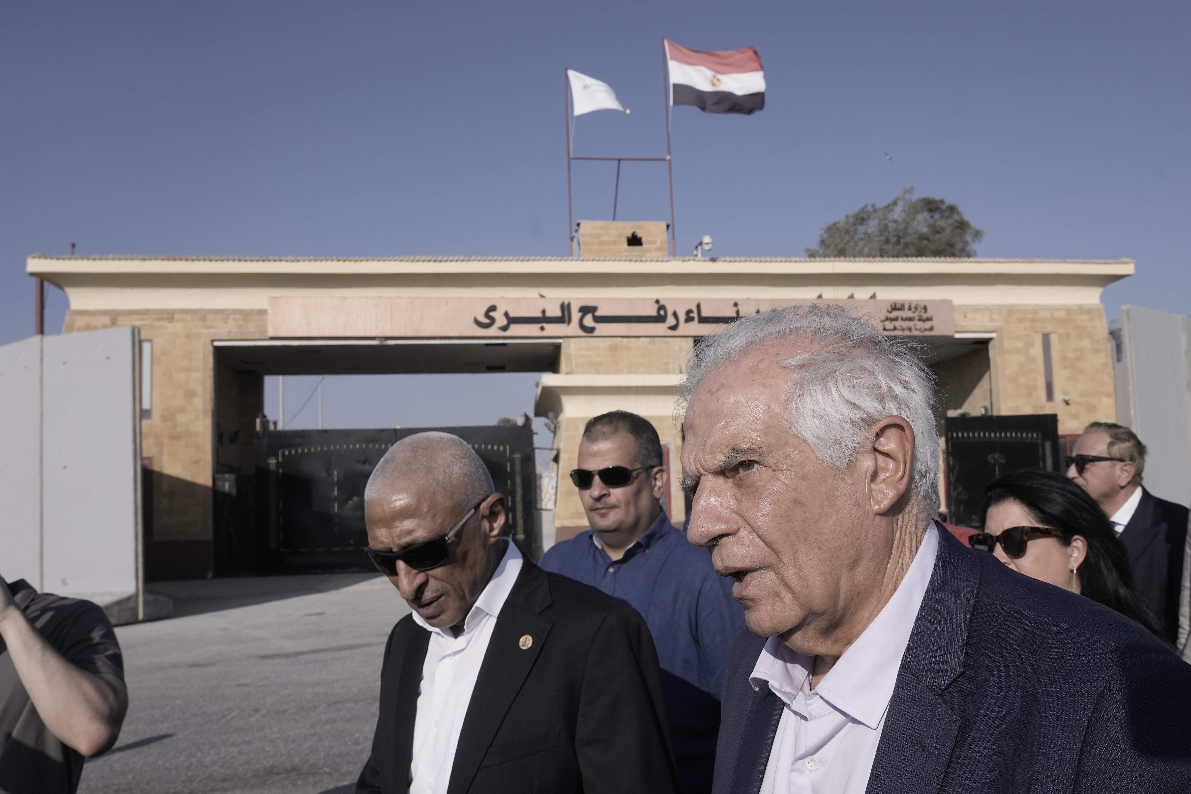 Josep Borrell läuft mit einer Gruppe von Menschen in Anzügen. Im Hintergrund ist der Grenzübergang Rafah mit der ägyptischen Flagge darauf zu sehen.