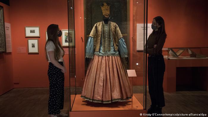 Eine Jacke aus goldenen Stoff, eine Bluse aus türkisfarbene Stoff und ein Rock aus lachsfarbenem glänzendem Stoff sind in der Ausstellung zu sehen.