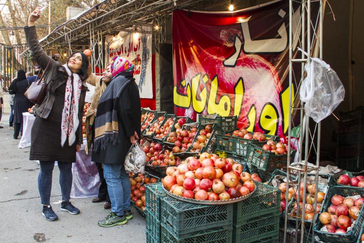 A group of women take a selfie in front of a pomegranate stall at a market (photo: Changiz M. Varzi)