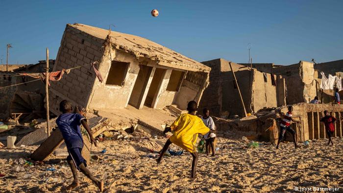 Children playing on beach with flood-damaged homes in the background on the coast of Senegal