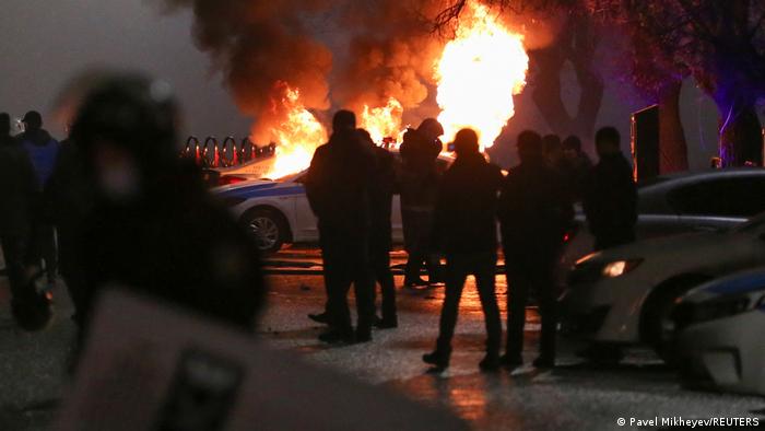 Protesters stand in front of a burning police car