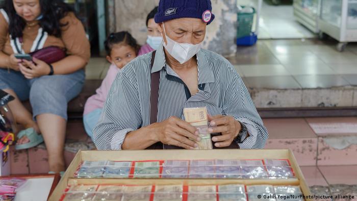 Man wearing mask has stack of bills wrapped in rubber band