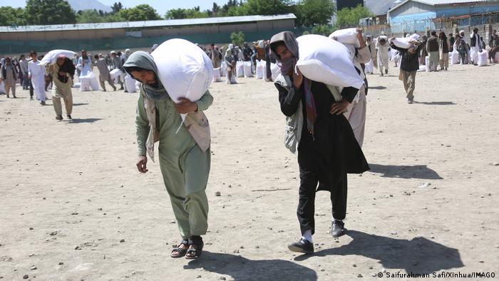  Männer in Kabul erhalten Lebensmittellieferungen aus China und tragen sie davon.