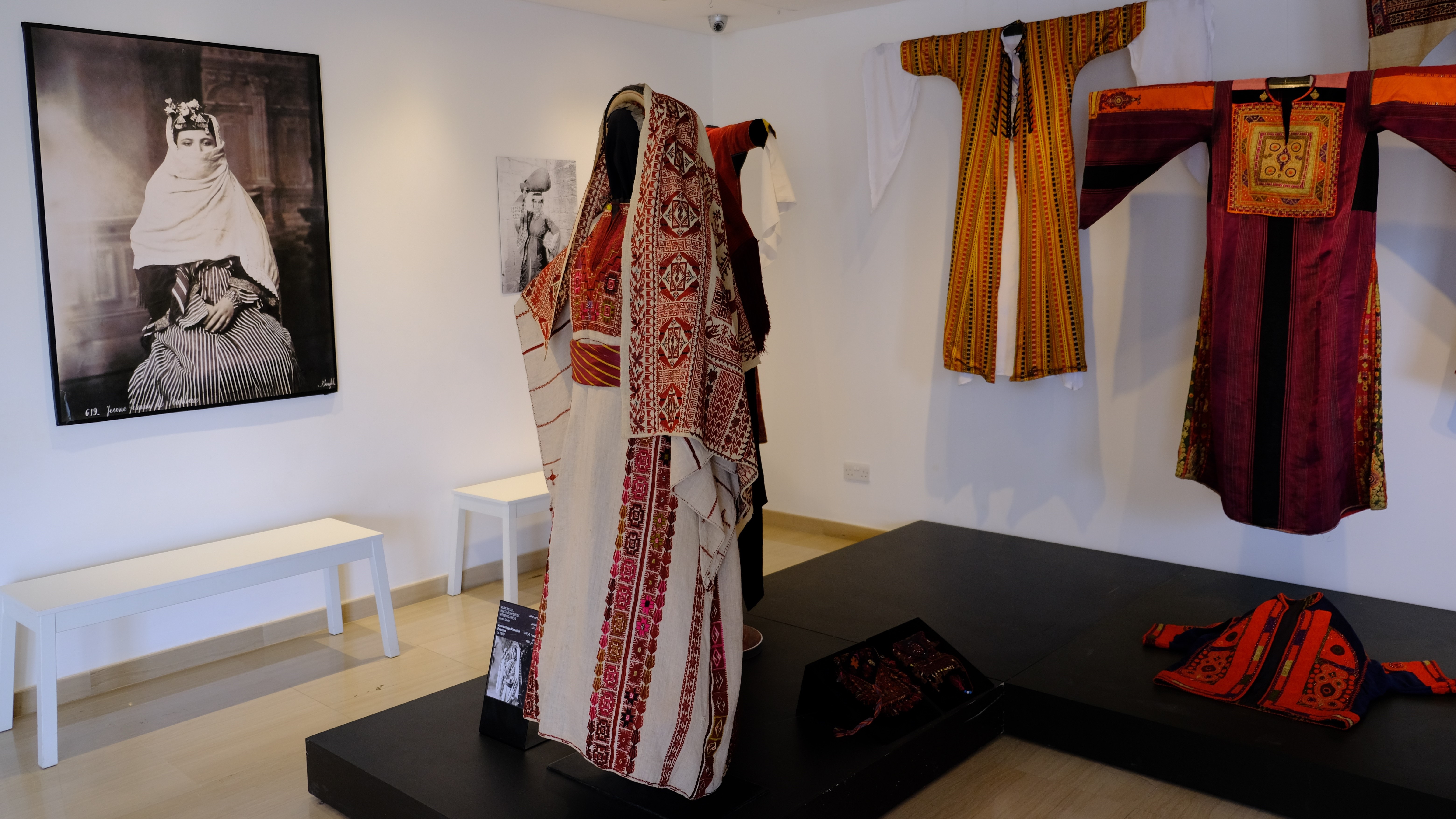 نماذج لأزياء بلاد الشام المطرزة المعروضة في متحف "طِراز" في الأردن. Exhibition space displaying Levantine costumes and an ancient photo of a women in traditional dress in Widad Kawar's Tiraz Museum (photo: Marta Vidal)