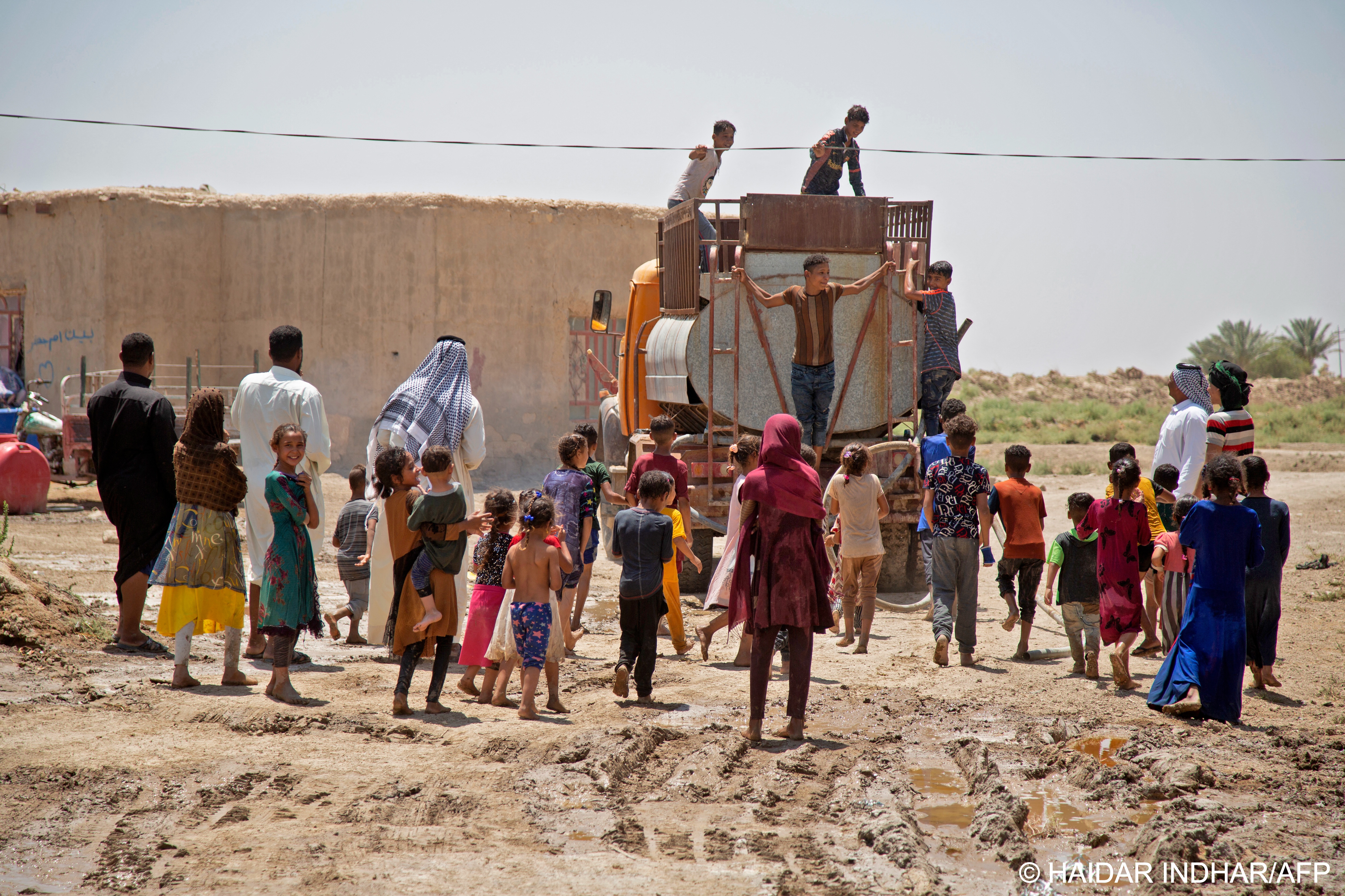 One person fills a tall white tank, climbing on top of it to hold the truck's hose as water gushes out, while others wait to fill smaller tanks or even cooking pots (photo: Haidar INDHAR/AFP)