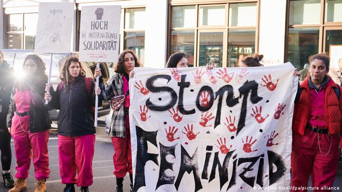 A line of women dressed in magenta hold up placards and a banner staying "Stop femicide"