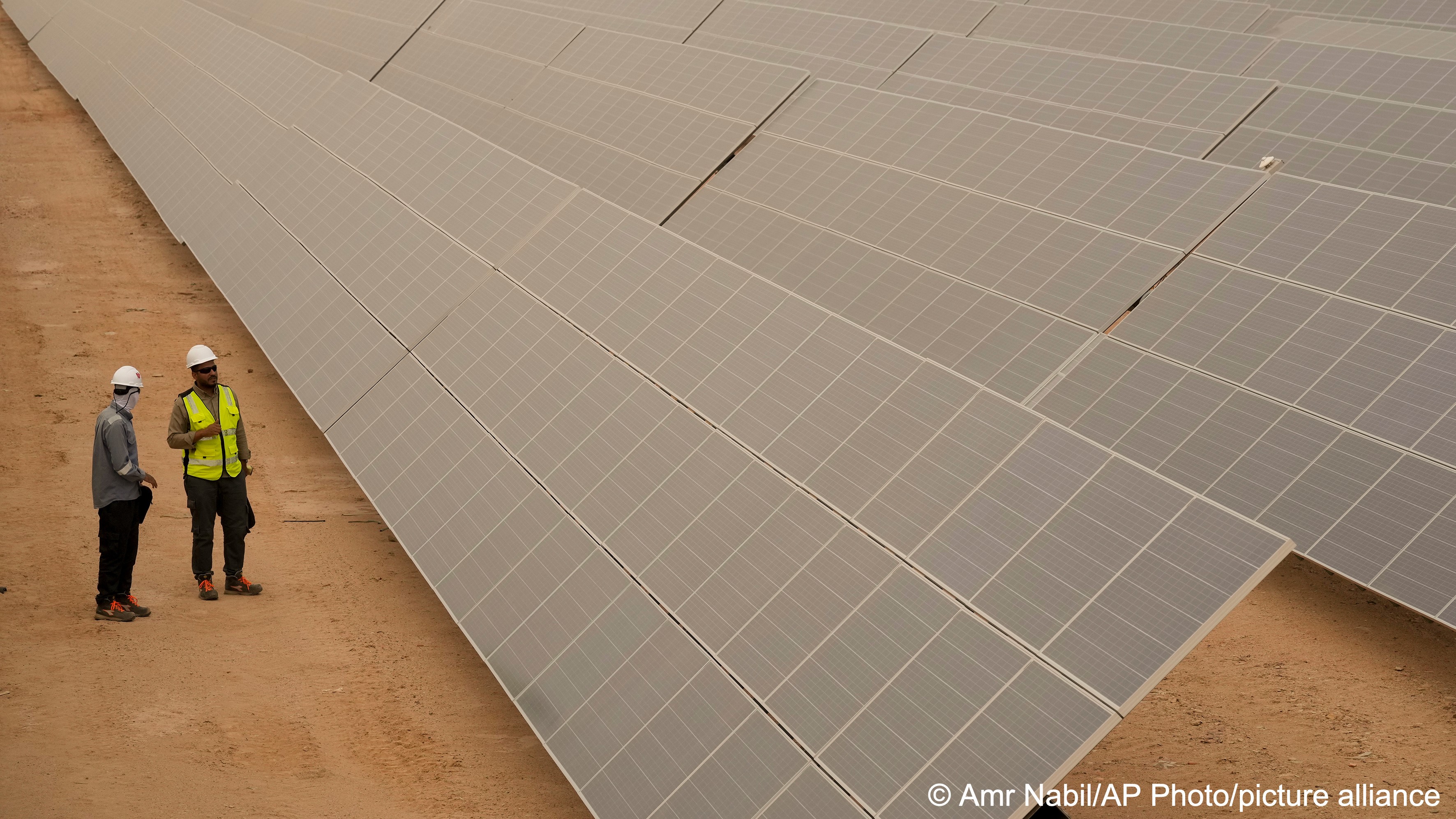 Engineers talk next to photovoltaic solar panels at Benban Solar Park, one of the world’s largest solar power plant in the world, in Aswan, Egypt, 19 October 2022 (photo: AP Photo/Amr Nabil)