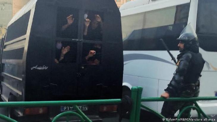 Women's hands are seen holding on to the wire mesh of the window in the back of a police van as an officer looks on (photo: SalamPix/abaca/picture alliance)