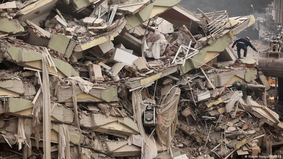 مبنى سكني أصبح كالعجينة بمدينة كهرمان مرعش بسبب زلزال تركيا. A person scrambles up a collapsed building in Kahranmanmaras, Turkey (image: Stoyan Nenov/REUTERS)