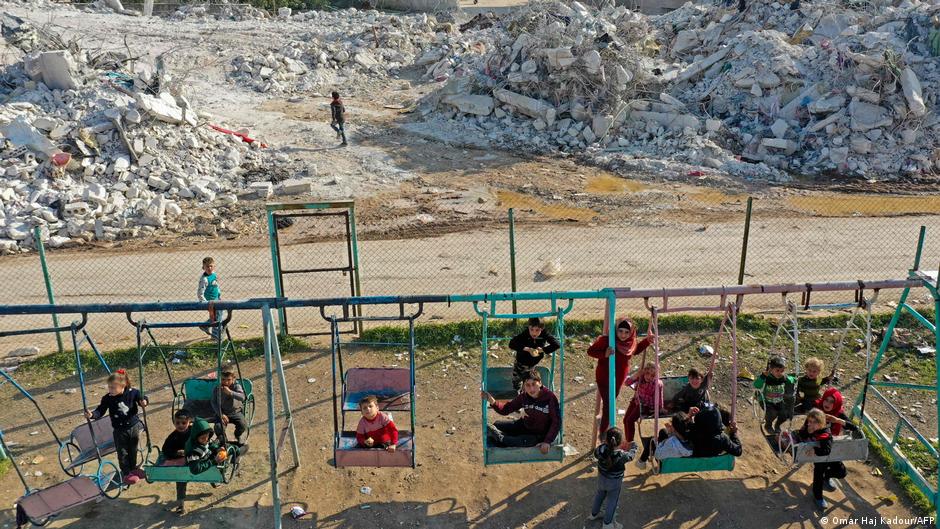 Children play on swings, in the background a street of rubble (image: AFP)