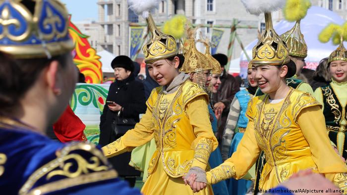 Laughing women wearing traditional yellow costumes dance hand in hand.