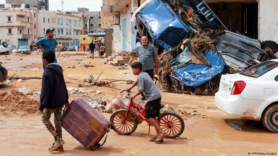 A young person wheels a suitcase though Derna