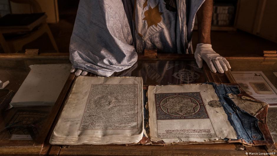 A person with gloves stands in front of an open old manuscript