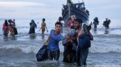 Refugees carry their belongings as they make their way ashore through the waves from a boat on the coast of Aceh, Indonesia, 16 November 2023