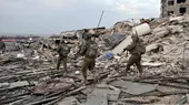 Three Israeli soldiers, armed and in fatigues, walk through rubble in the Gaza Strip 