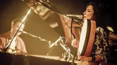 Djazia Satour (right) sings into a microphone as she plays the bendir; in the background, sitting at a grand piano, is pianist Pierre-Luc Jamain