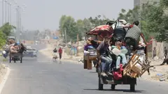 Junge Menschen in Gaza sitzen auf einem mit Möbeln und anderen Habseligkeit bepacktem Karren und verlassen die zerstörte Stadt
