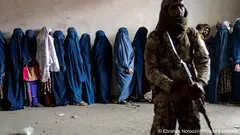 أحد أعضاء حركة طالبان يحرس نساء مصطفات للحصول على إمدادات إغاثة.